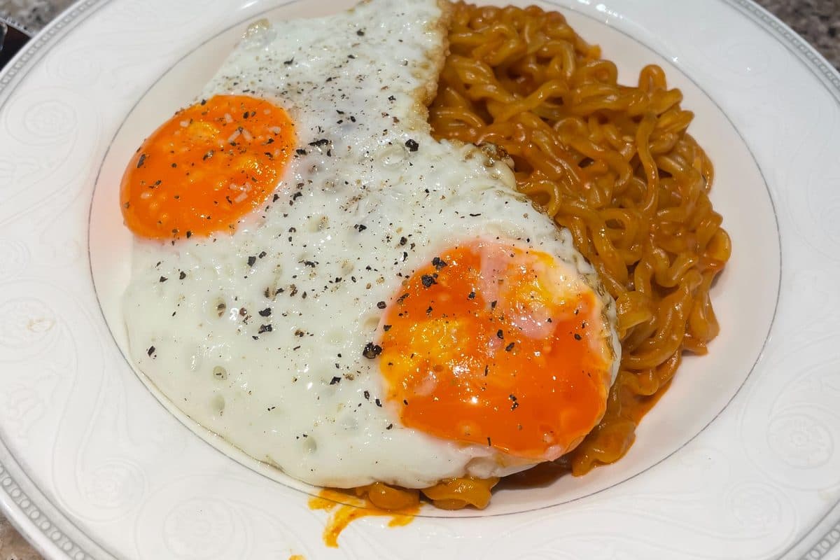 Fried eggs with spicy noodles on a white plate