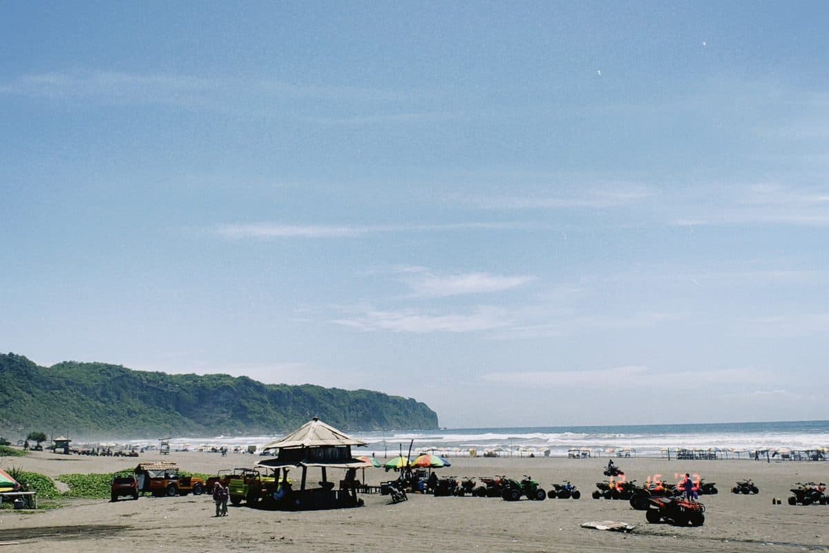 A wide beach with ATVs and green cliffs